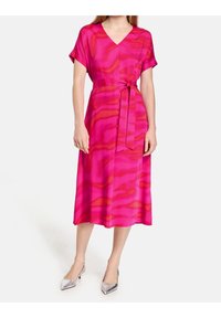Fuksjowa sukienka z dekoltem w serek i krótkimi rękawami, z wiązaniem w talii. Tkanina ma falisty wzór w ciemniejszych odcieniach różu.