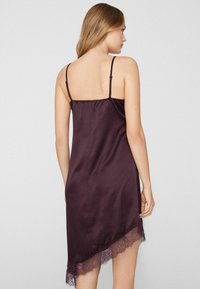 Camisón de satén en púrpura intenso con finas tirantes ajustables y encaje en el dobladillo asimétrico, con una textura suave.