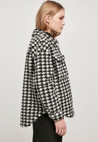 Over-size jakke i houndstooth-mønster i sort og hvid, med krave og to brystlommer, lavet af et blødt, struktureret stof.