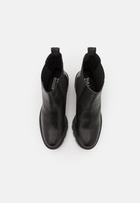 Stivali alla caviglia in pelle nera con pannelli laterali elastici, punta arrotondata e suole in gomma testurizzata. Presentano un pratico cinturino per un facile indossamento.