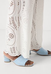 Mule aperti azzurri con tacco a blocco. Realizzati in materiale liscio, presentano un design minimalista. Abbinati a tessuto bianco ricamato.