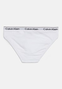Λευκά εσώρουχα μπικίνι Calvin Klein με ελαστική μέση με λογότυπο σε απλό φόντο.