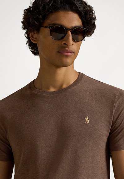 Καφέ κοντομάνικη μπλούζα από βαμβάκι, με μικρό κεντημένο χρυσό λογότυπο στην αριστερή πλευρά του στήθους. Υφή υφάσματος με λαιμόκοψη τύπου crew.