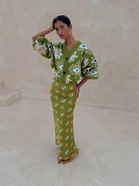 Cardigan en maille vert avec motifs d'œil et de soleil ; assorti à une jupe verte arborant des motifs similaires. Des chaussures à talons marron complètent la tenue.