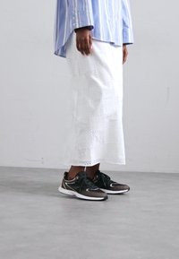 White knee-length skirt with eyelet pattern and a straight cut, paired with black athletic shoes featuring white accents and laces.