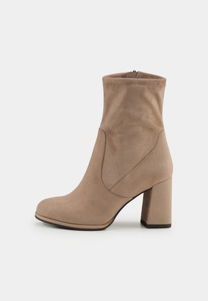 Beige Wildleder-Ankle Boots mit runder Zehenbox, Blockabsatz und engem Schaft, ausgestattet mit Ziernähten und einem Reißverschluss hinten.