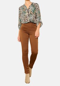 Blusa stampata con motivi animalier in verde e beige, abbinata a pantaloni aderenti marroni. L'outfit include stivaletti beige alla caviglia.