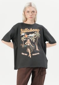 Svart overdimensjonert t-skjorte med grafisk design av en hula-danser og palmer, med en vintage-stil logo og tekst nederst.