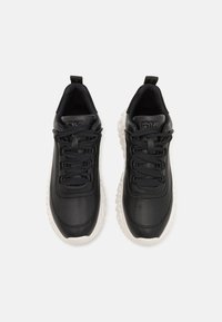 Scarpe sportive nere con tomaia in pelle liscia, lacci piatti e suola bianca texturizzata. Presentano un marchio in rilievo sulla linguetta.