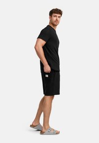 Schwarzes, strukturiertes T-Shirt und passende Shorts. Die Shorts haben eine Seitentasche und ein Etikett. Helle graue Sandalen runden das Outfit ab.