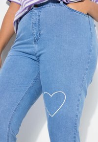 Ljusblå denimjeans med en figursydd design, som har en broderad vit hjärtdetalj på vänster lår. Slät textur och klassisk passform.