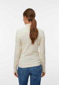 Suéter de cuello alto beige con mangas largas, puños acanalados y dobladillo, combinado con jeans de mezclilla azul, mostrado desde la parte trasera.
