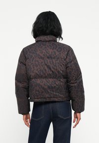 Veste doudoune à imprimé léopard marron foncé et noir. Elle dispose d'un col haut et d'un design court avec des manches bouffantes pour plus de chaleur.