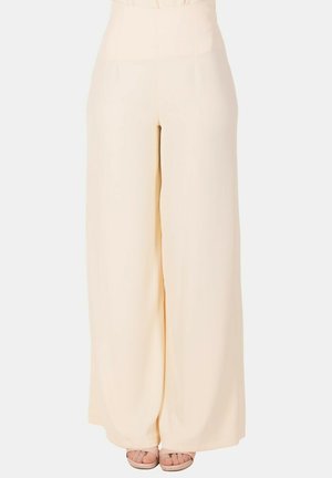 Pantaloni crema a gamba larga e vita alta, indossati con sandali nudi a punta aperta, mostrati dalla vita ai piedi su sfondo bianco.