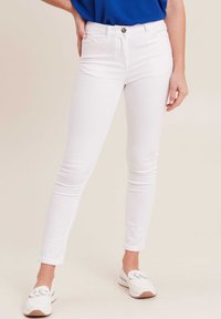 Witte skinny jeans met een gladde textuur, voorzien van een knoop aan de voorkant en zakken. Draag ze met een blauwe top en witte instappers.