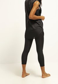 Czarny sportowy top bez rękawów z siateczkowymi detalami, w połączeniu z czarnymi legginsami do połowy łydki. Obydwa elementy mają gładką fakturę.
