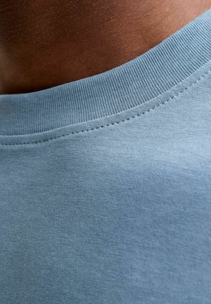 Camisa azul claro de manga corta con un cuello acanalado. La tela tiene una apariencia suave y texturizada con detalles de costura fina.