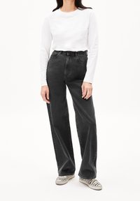 Zwart denim jeans met hoge taille, losse pasvorm en riemlussen, gecombineerd met een wit langermig overhemd en gestreepte instappers.