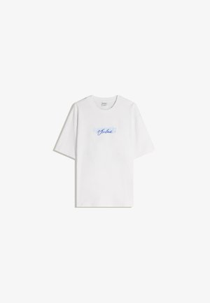 Tricou alb din bumbac cu o croială relaxată, având un text grafic de culoare albastră deschisă care spune "Valoare" în scris cursiv pe piept.