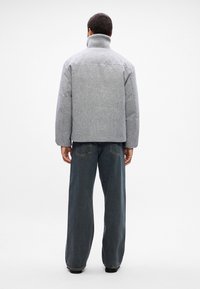 Šedá péřová bunda s vysokým límcem, texturovaným materiálem a volným střihem. Spárovaná s džínami s širokými nohavicemi. Minimalistický design, bez viditelných log.