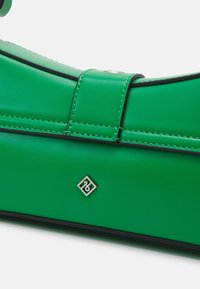 Vihreä tekonahkainen käsilaukku, jossa on sileä pinta, ja joka on varustettu erottuvalla mustalla tikkausompeleella sekä pienellä hopeisella logolla.