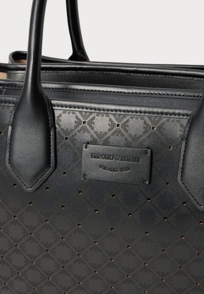 Černá taška Emporio Armani přes rameno s perforovaným geometrickým vzorem a prošitými koženými uchy, logo značky na přední straně.