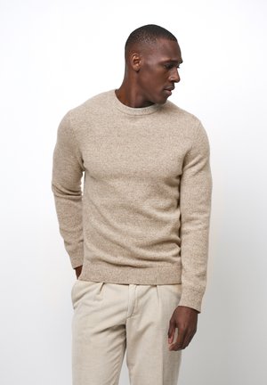 Beige knit sweater with a round neckline and long sleeves, made of textured fabric. Worn with light beige corduroy trousers.