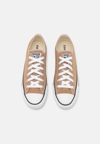 Hnědé plátěné tenisky s bílými tkaničkami, gumovými špičkami a černým lemem. Obsahují štítek s nápisem "Converse" a hvězdičkovým logem na jazyku.