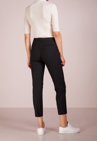 Svarta skräddarsydda byxor med smal passform, som har rena linjer och sidofickor, ihop med en ljusbeige ribbad tröja och vita sneakers.