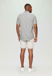 Korte mouwen, geknoopte blouse in een groen en wit patroon, gecombineerd met beige opgerolde shorts en witte sneakers. Achteraanzicht weergegeven.