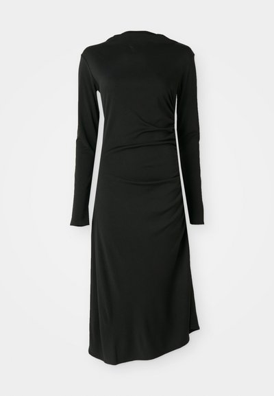 Robe noire à manches longues avec une silhouette ajustée et un détail froncé sur les côtés. Fabriquée en tissu extensible et lisse, avec un col rond modest.