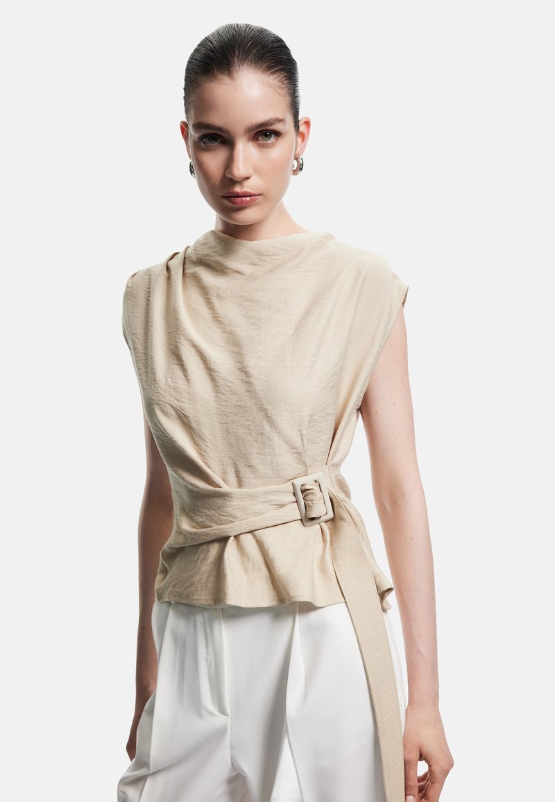 Beige Leinenoberteil mit hohem Kragen, seitlichen Drapierungen und einem Bindegürtel in der Taille; zeichnet sich durch ein minimalistisches Design mit weicher Textur aus.