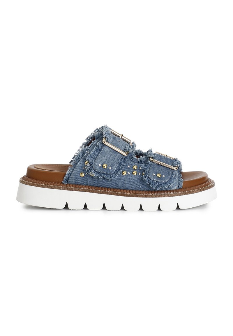 Sandali scivolati in denim con bordi sfilacciati, doppie fibbie argentate e borchie dorate su una soletta marrone con una suola spessa bianca.