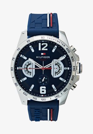 Herrearmbåndsur med et marineblåt gummirem, sølvurcase, mørk urskive og hvide detaljer. Udstyret med store tal, tachymeter og to subcirkler.