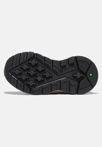 Semelle de chaussure en caoutchouc noir avec un motif de semelle, comportant des éléments de grip et de traction. Un accent vert est visible près de la zone du talon.