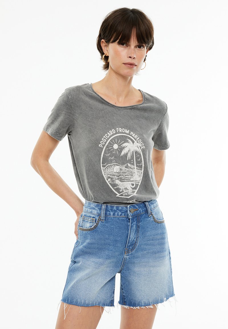 Camiseta de algodón gris con cuello redondo y un estampado gráfico blanco. Combinada con pantalones cortos de denim azul claro con dobladillos deshilachados y bolsillos frontales.