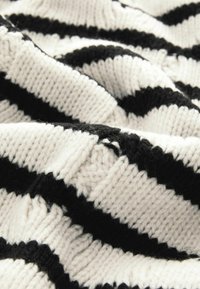 Tissu tricoté avec des rayures noires et blanches ; présente une texture douce et des points visibles ; inclut une légère effilochure dans le motif.