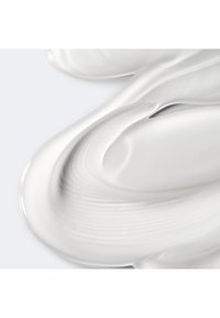 Hvit krem eller lotion med tekstur av jevne, flytende kurver og rygger, som ser tykk og blank ut mot en lys bakgrunn.