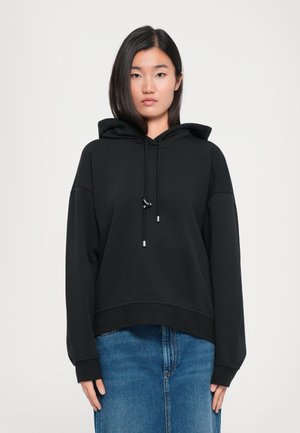 Sweatshirt à capuche noir avec une coupe décontractée, des manches larges et des accents de cordon de serrage. Associé à une jupe en denim bleue.