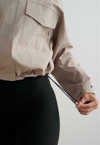 Svijetložuti, dugih rukava, s džepovima na prsima, majica s podesivim šniranjem na donjem dijelu, u kombinaciji s crnim rebrastim tajicama. Minimalistički dizajn, elegantna tkanina.