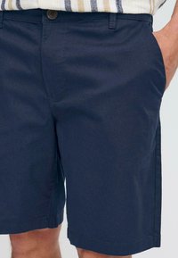 Shorts bleu marine en tissu léger, dotés de poches et d'une fermeture à bouton. Le design est simple avec une coupe droite et des coutures nettes.