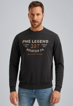 Schwarzer Baumwollpullover mit Rundhalsausschnitt und gerippten Bündchen. Vorderseitiger Grafiktext in Beigetönen und Gold. Legere Passform.