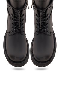 Paire de bottes en cuir noir à lacets avec semelles épaisses et fermetures éclair latérales, vues de dessus sur fond blanc.