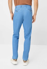 Chinos azzurri chiari con una vestibilità slim, dotati di due tasche posteriori con chiusura a bottone e un tessuto liscio e strutturato. Abbinati a sneakers bianche.