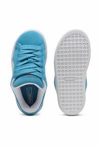 Tirkizne zamšaste tenisice s bijelim potplatima i vezicama. Teksturirani gumeni potplat ima kružne uzorke. Puma logo vidljiv na jeziku.