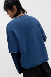 Blauer übergroßer Pullover mit rohem Saum und sichtbaren Nahtdetails, gefertigt aus weichem Baumwollstoff. Verfügt über eine lockere, kastige Passform.