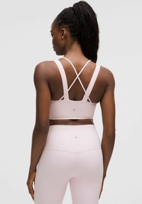 Light pink athletic bra with crisscross straps, smooth texture, and logo on the back, paired with matching high-waisted leggings.