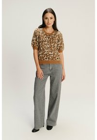 Karmelowy sweter w leoparda z dzianiny, z krótkimi bufkami i okrągłym dekoltem, zestawiony z szarymi spodniami o szerokich nogawkach i czarnymi butami.