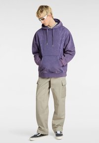 Purple hooded sweatshirt with a front pocket, grey interior, and subtle pattern. Paired with light beige cargo pants and black sneakers.