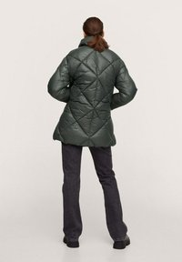 Grøn quiltet pufferjakke med høj krave, der har et diamantmønster. Jakken har en længere pasform og er parret med mørke jeans.
